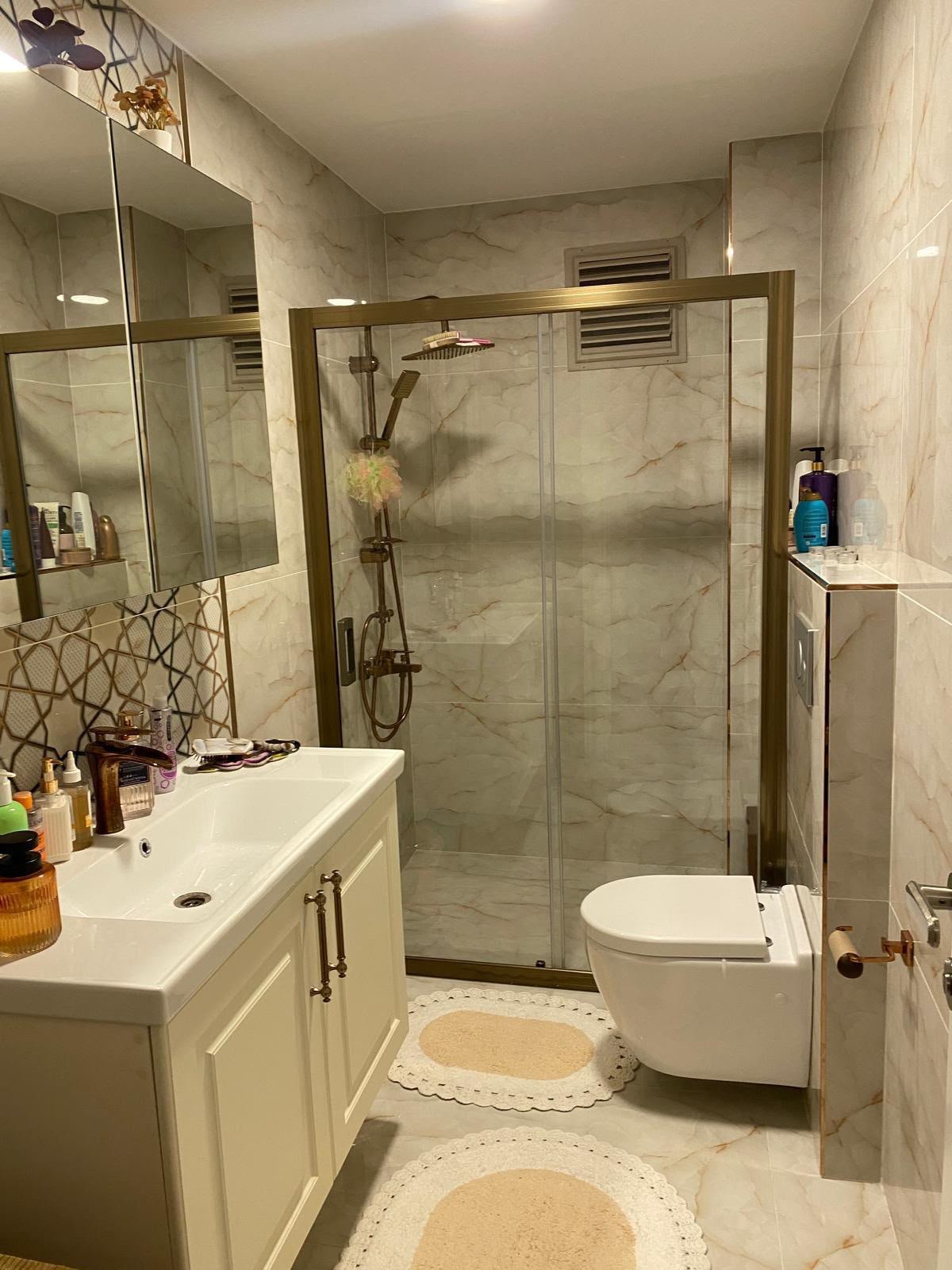 Bronz duş kabini, krem lavabo dolabı ve mermer görünümlü banyo